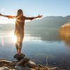 Young cheerful woman by the lake enjoying nature. Arms outstretched for positive emotion.